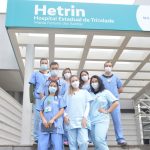 Alunos de medicina, entre meninas e meninos estão à frente do hospital Hetrin nas escadas com roupas no tom azul claro, todos participam do Programa de Estágio Hetrin